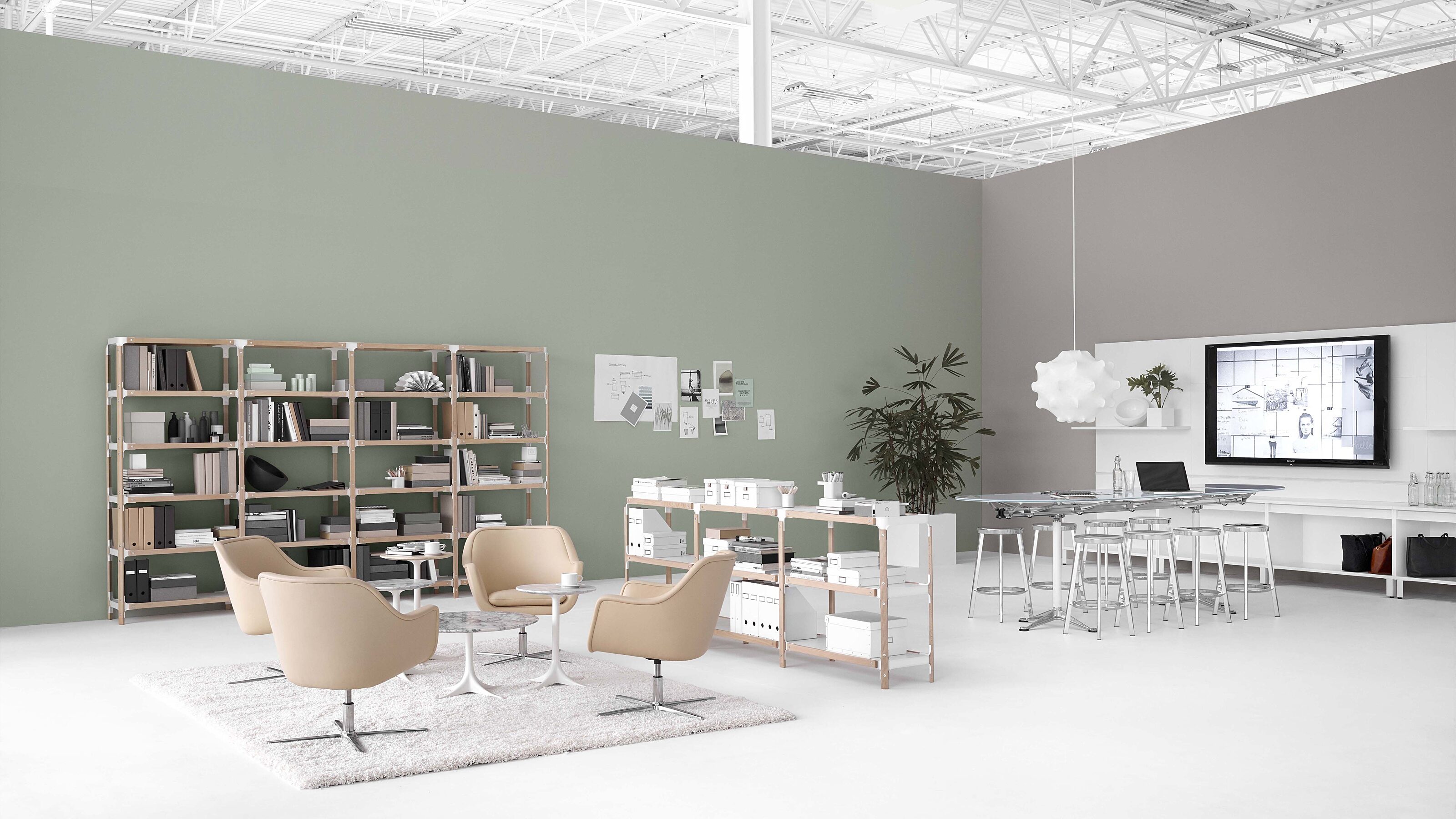 open plan office space. Left hand side with simple tan lounge chairs. Right side with a high top conference table and metal stools, tv on far right wall.